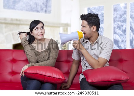 Portrait of angry man using a megaphone for scolding his wife at home