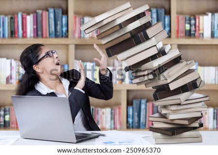 Young student of business management hold a pile of falling books in the library