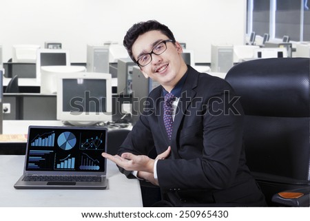 Portrait of caucasian worker showing financial chart on laptop computer while smiling friendly