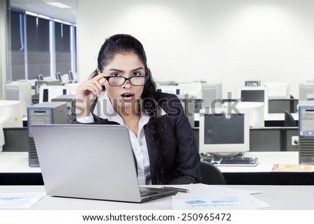 Portrait of shocked indian businesswoman looking at the camera through her glasses in the office