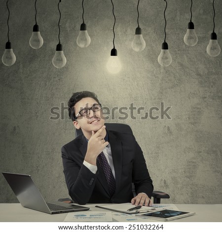 Caucasian worker in business suit working on desk while looking up at bright lightbulb