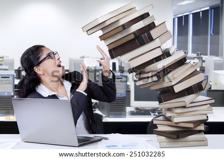 Worried employee hold a pile of falling books in the office, symbolizing task for work overtime