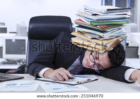 Caucasian businessperson sleeping in the office with documents on his head, shot in the office
