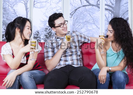Group of multi ethnic teenagers sitting on sofa while drinking beer, shot at home in winter day