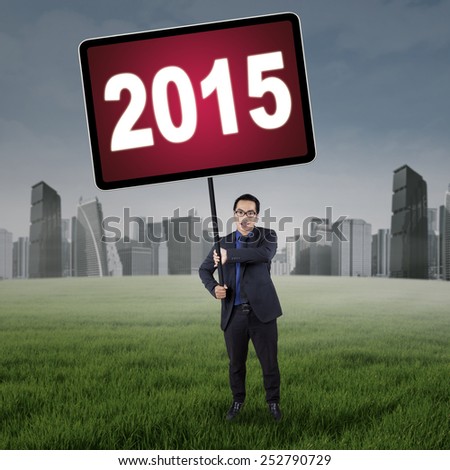 Male entrepreneur standing on the field while holding a board with number 2015