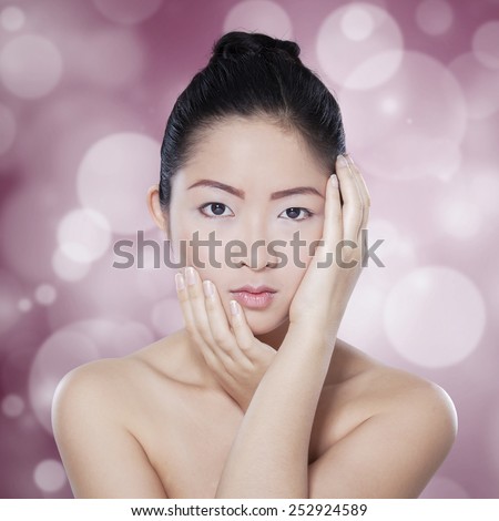 Portrait of beautiful chinese woman with clean skin after skin care, shot against light glitter background