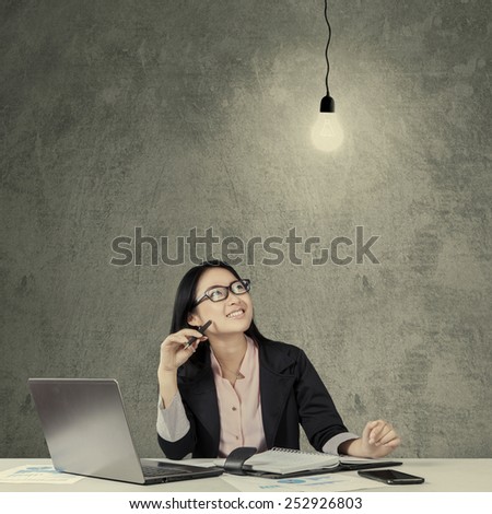 Young chinese businesswoman working at table while smiling happy and looking at lightbulb