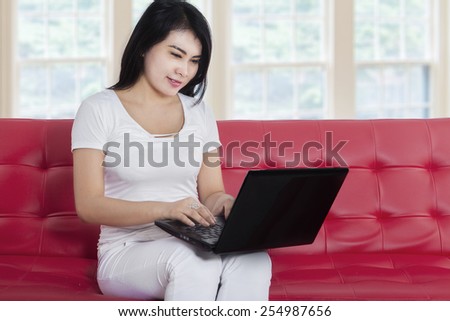 Young asian woman using laptop computer while sitting on cozy sofa at home
