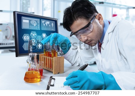 Portrait of young scientist writes the report of observation result on the clipboard, shot in the laboratory