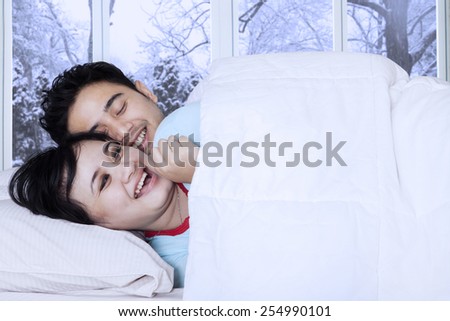 Joyful couple lying on bed and joking together with winter background on the window