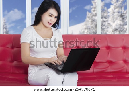 Young woman with casual clothes sitting on cosy couch while using laptop computer