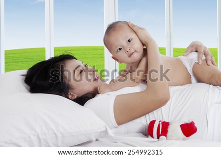 Happy mother playing with her little daughter on bed with summer background on the window