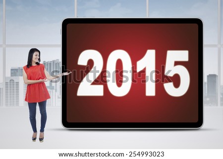 Full length of casual businesswoman standing in the office while showing numbers 2015 on a board