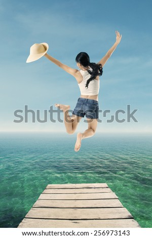 Rear view of attractive woman with short pants jumping on the pier at tropical beach