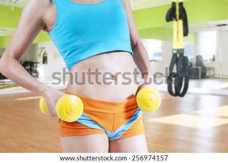 Close up of muscular woman tummy in the fitness center while workout with two dumbbells