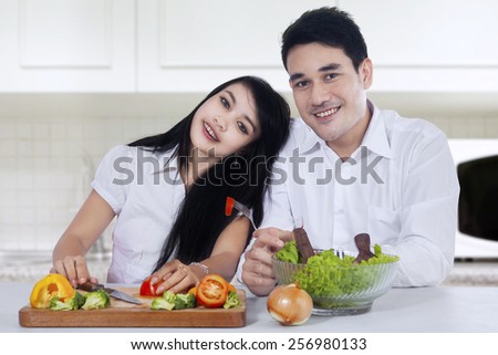 Portrait of happy couple with vegetables salad sitting in the kitchen while smiling at the camera