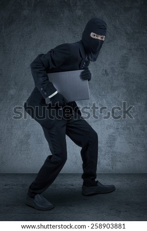 Male worker wearing mask sneaking to steal a laptop computer