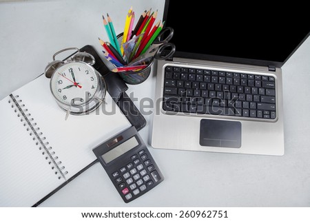 High angle view of office table with laptop, calculator, alarm clock, and stationery
