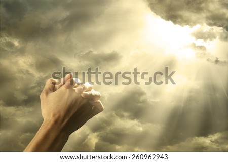 Closeup of prayer raised hands on the sky with bright rays from the cloud