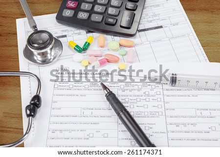 Health insurance claim form with drugs, injection, pen, stethoscope, and calculator on the table