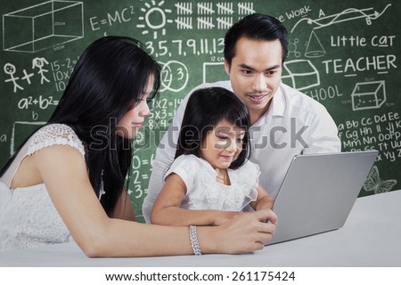Two parents help their daughter to study by using a laptop computer on the table