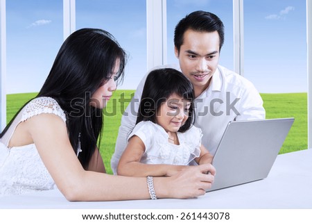 Little girl using a laptop computer on the table with her parents, shot at home