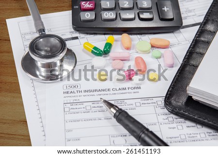 Closeup of health insurance claim form with pen, stethoscope, drugs, calculator, and notes