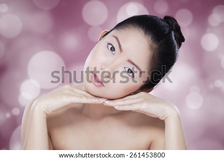 Portrait of chinese female model with black hair and fresh skin, looking at the camera against light glitter background