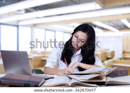 Portrait of young nerdy student studying with textbooks and write quotations on a book in the class