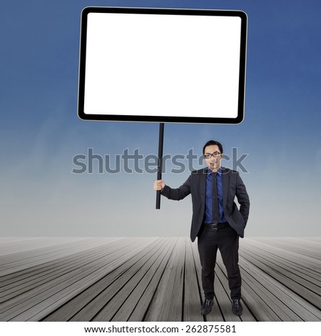 Full length of businessman wearing formal suit and standing on the wooden floor with blank billboard