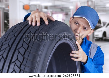 Young asian technician with a blue workwear checking a black tire in the workshop