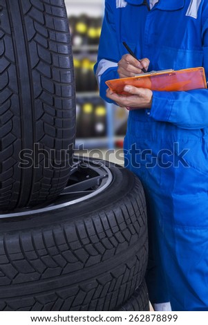 Male technician working at workshop while checking the tires condition and writes the report
