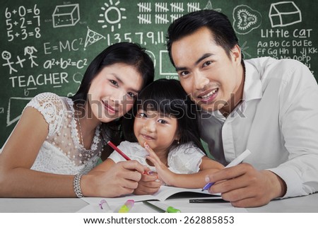 Little family smiling at the camera while studying together, shot with scribble background on the blackboard