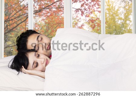 Asian couple sleeping together in bedroom with autumn background on the window
