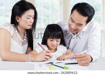 Little girl writing on book while helped by her parents at home