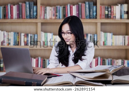 Portrait of clever student studying in the library and use a laptop computer