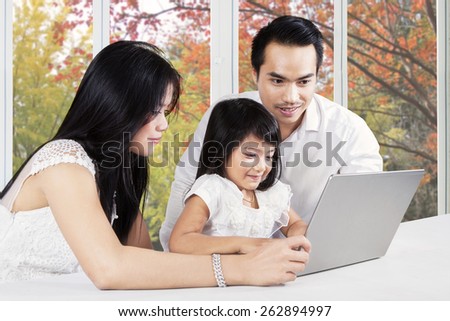 Portrait of modern parents teaching their daughter with a laptop on table, shot at home