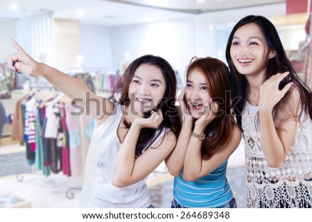 Group of cheerful teenage girls having fun in the shopping center and look at a store