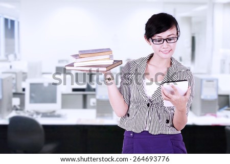 Smiling businesswoman using digital tablet with books on her hand at office