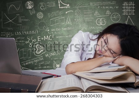 Beautiful teenage schoolgirl sleeping on desk over textbooks and looks tired after studying
