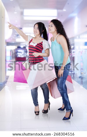 Pretty asian girls holding shopping bags while looking at a store together, shot in the shopping center