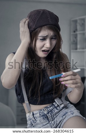 Portrait of shocked teenage girl sitting in the bedroom while holding a pregnancy test with unwanted pregnancy result