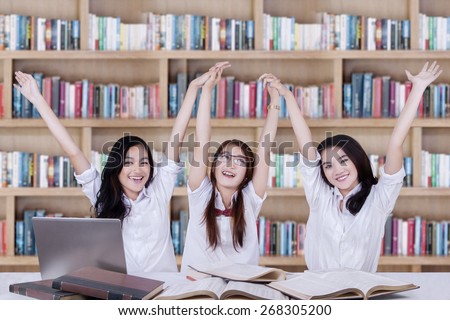 Happy high school students studying in the library and raise hands together