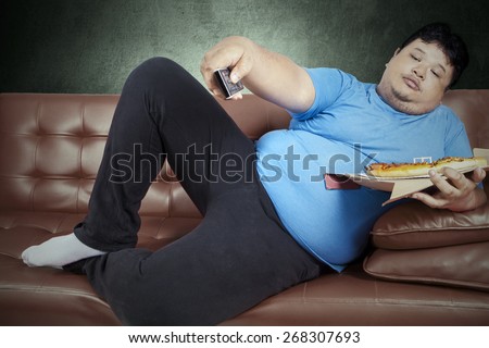 Overweight man eats pizza while sitting on couch at home