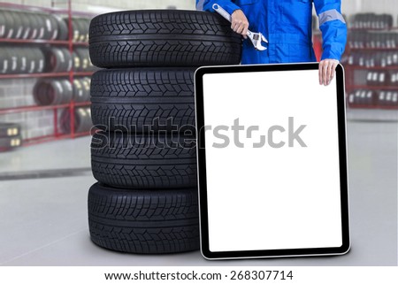 Male mechanic standing in the workshop while lean on tires and holding a blank placard