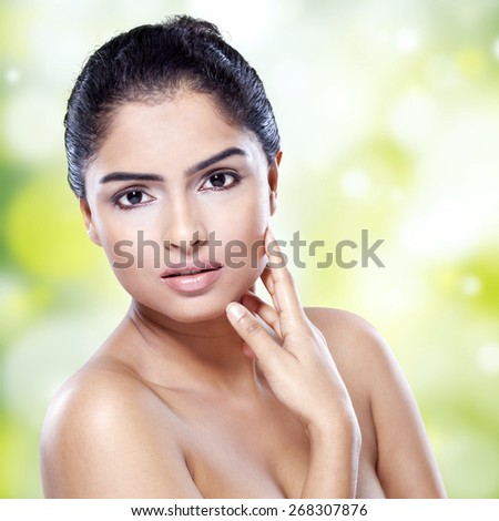 Portrait of young woman with black hair, pretty face, and perfect skin looking at camera against bokeh background