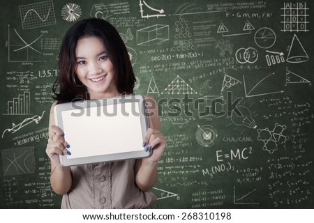 Lovely young high school student standing in the class and showing a blank tablet screen