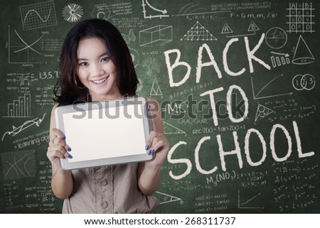 Beautiful teenage girl back to school and showing a blank tablet screen in the class
