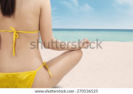 Back view of female model doing meditation while sitting at the beach
