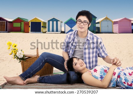 Attractive asian couple picnic at coast while sitting on mat and smiling at the camera